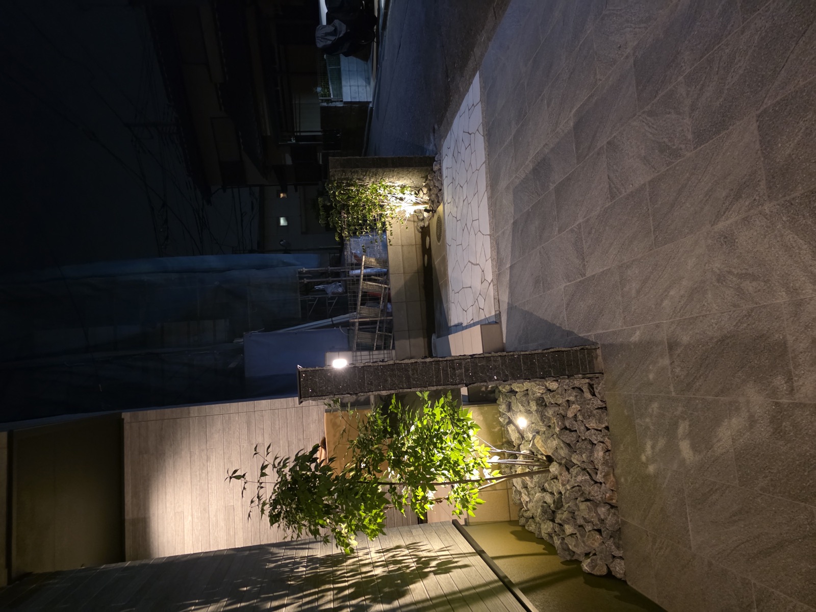 夜の志木市の玄関まわり。門柱の脇の植栽を照明が照らし、壁に枝葉の影が映る
